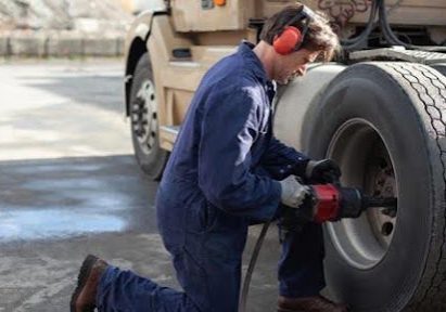Mechanic wearing ear protection using air compressor drill to bolt a new tire to a a semi-truck© Fangxianuo/Getty Images